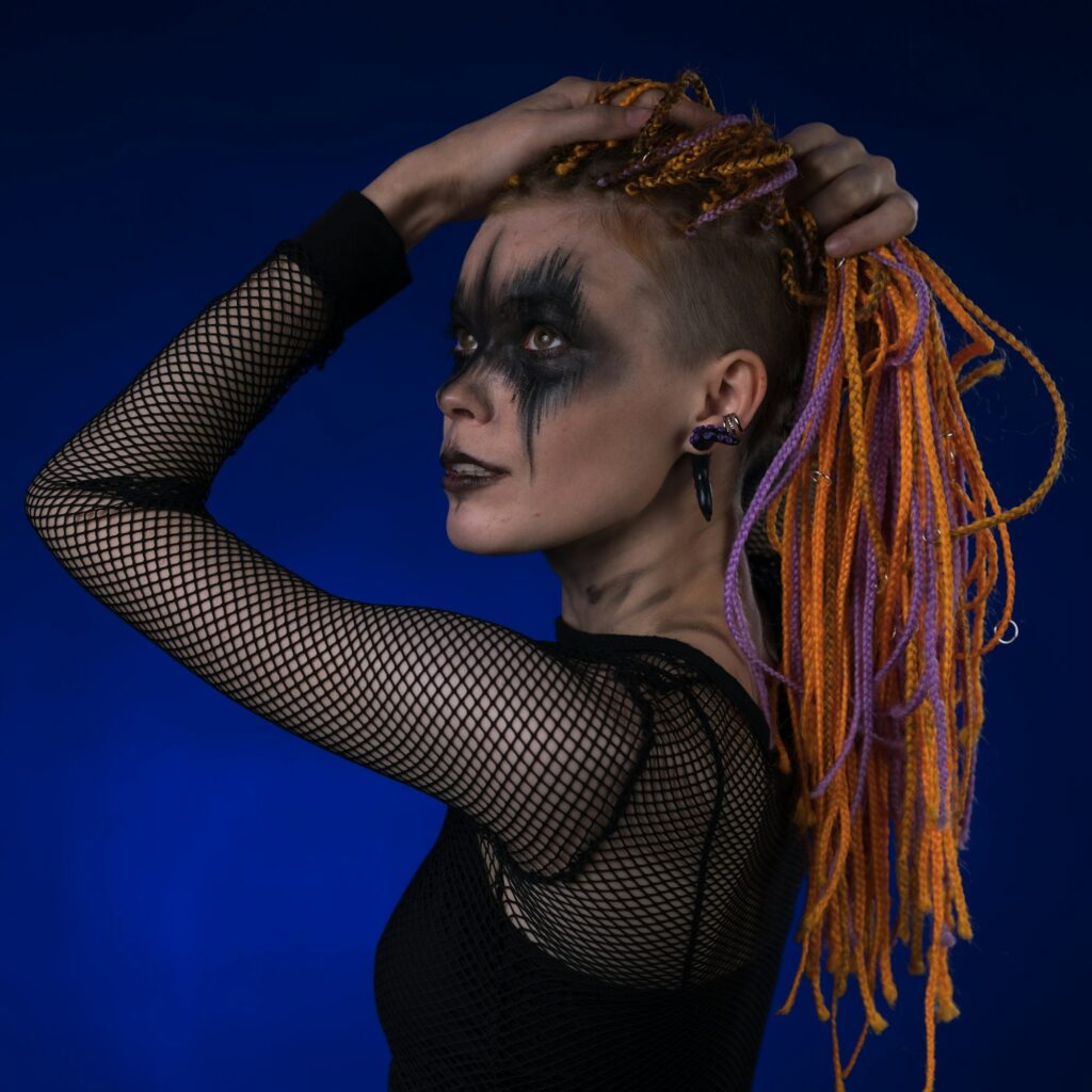 Dramatic portrait of young female with spooky stage makeup painted on face and dreadlocks hairstyle